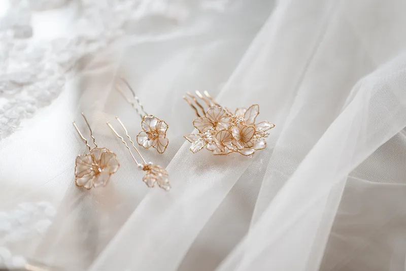 Peigne et épingles à cheveux aux fleurs nacrées et fils dorés, déposés sur un voile ivoire