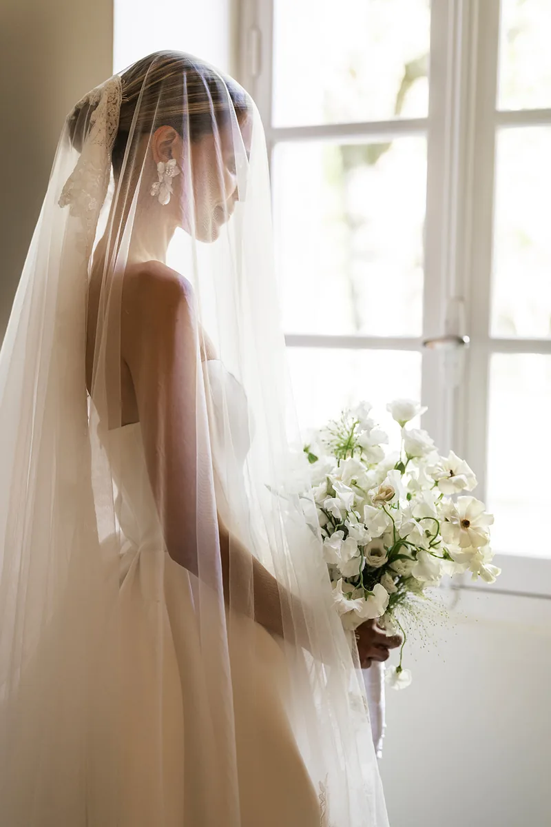 Boucles d’oreilles florales blanches portées sous un voile, près d’une fenêtre